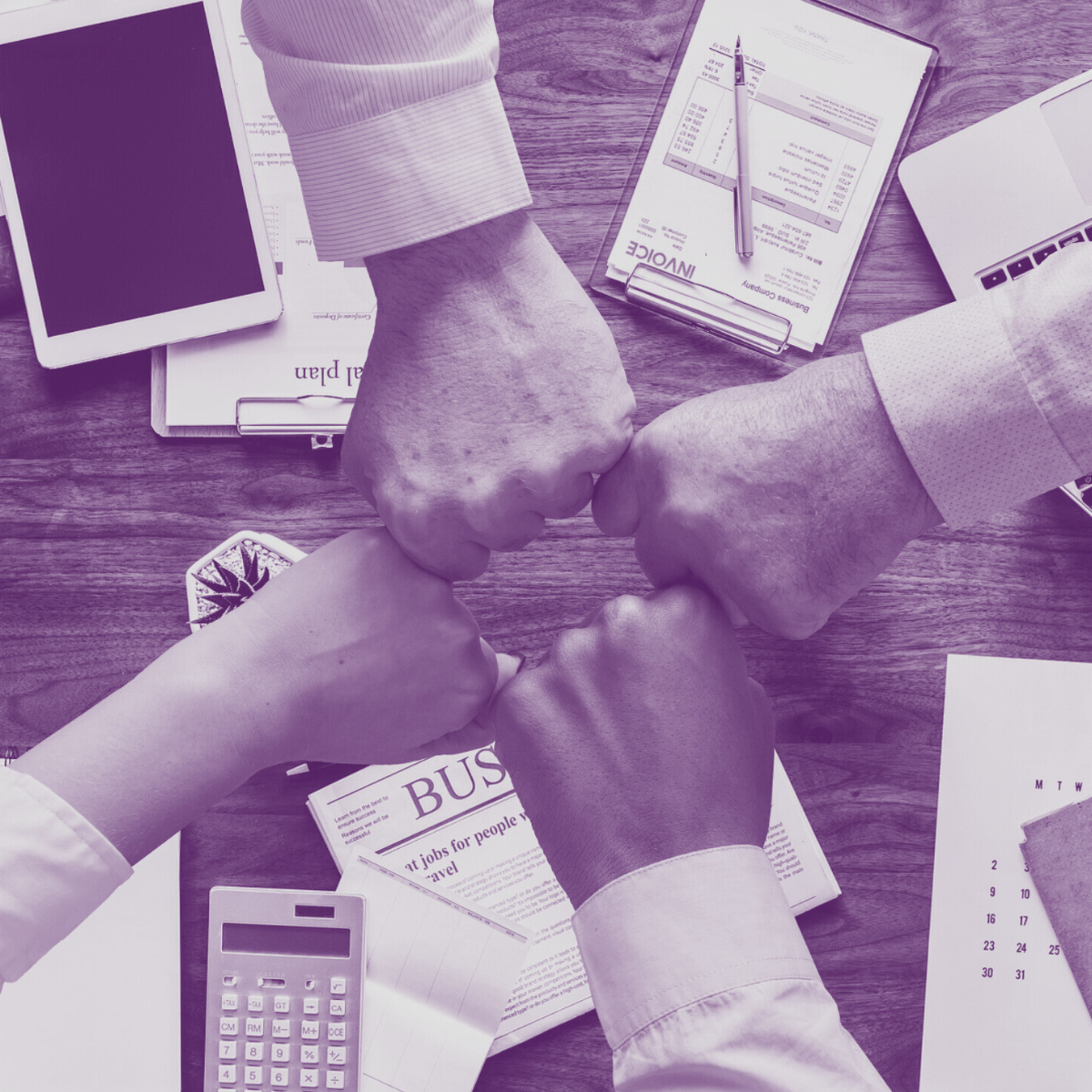 Four hands a fist-pumping over a table, which is covered in calculators, notes and technology